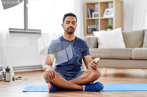 Image of indian man with smartphone on exercise mat at home