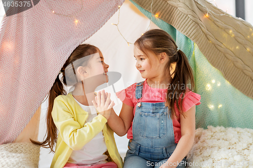 Image of happy girls lying in kids tent and talking at home