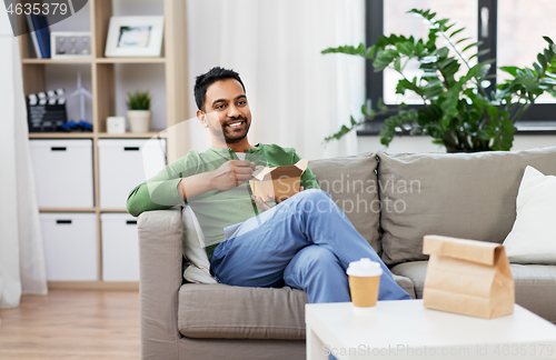 Image of smiling indian man eating takeaway food at home
