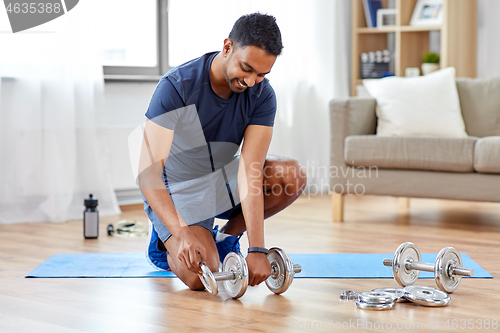 Image of smiling indian man assembling dumbbells at home