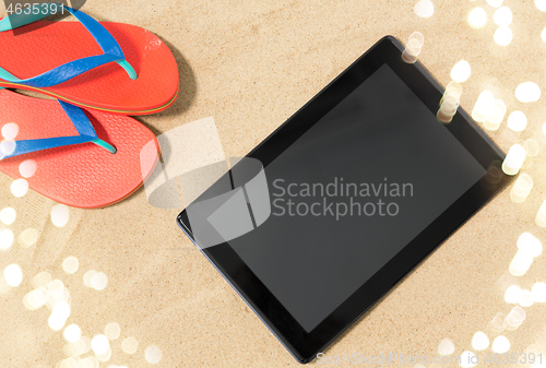 Image of tablet computer and flip flops on beach sand