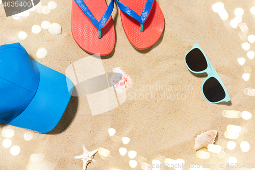 Image of cap, flip flops, shades and on shells beach sand