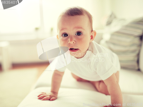 Image of little baby in diaper crawling along sofa at home