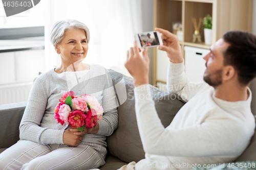 Image of adult son photographing senior mother at home