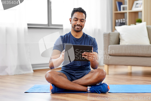 Image of indian man with tablet pc and exercise mat at home