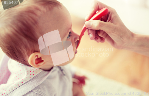 Image of hand with spoon feeding little baby at home