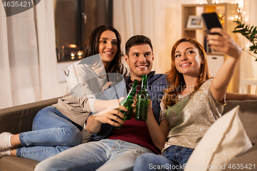 Image of friends clinking drinks and taking selfie at home