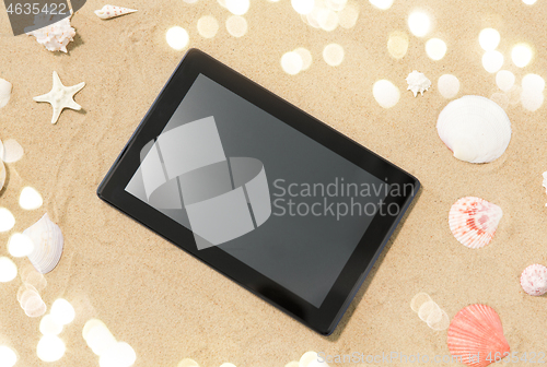 Image of tablet computer and seashells on beach sand