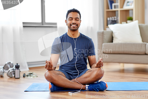 Image of indian man meditating in lotus pose at home