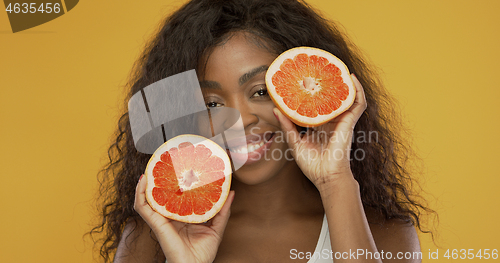 Image of Cheerful black lady showing halves of grapefruit