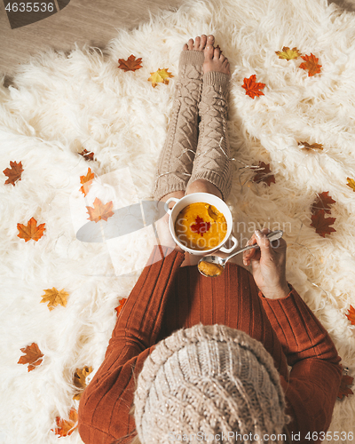 Image of Woman holds a bowl of spiced pumpkin soup sitting on cozy rug