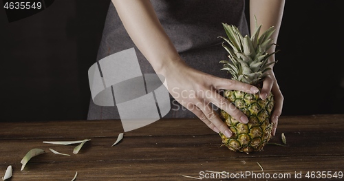 Image of Woman\' hands with ripe juicy natural organic tropical fruit pineapple on a wooden kitchen table on a black background.