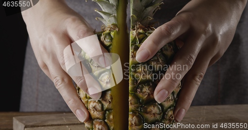 Image of Close up view. Woman\'s hands hold two pieces of juicy fresh natural organic pineapple on a wooden background.