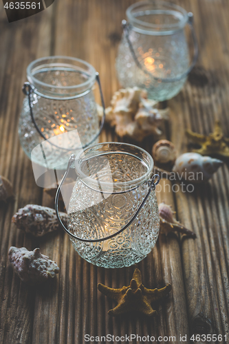 Image of Three vintage lantern with sea shells on wooden table