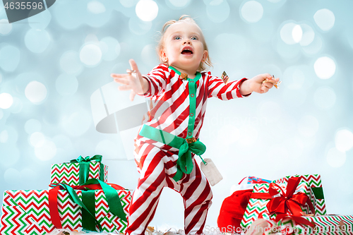 Image of Cute baby girl 1 year old wearing santa hat posing over Christmas background. Sitting on floor with Christmas ball. Holiday season.