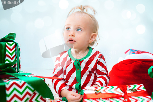 Image of Cute baby girl 1 year old near santa hat posing over Christmas background. Sitting on floor with Christmas ball. Holiday season.