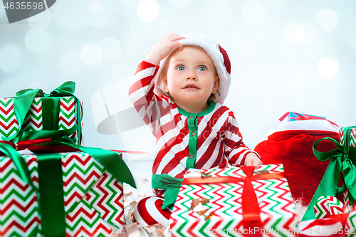 Image of Cute baby girl 1 year old wearing santa hat posing over Christmas background. Sitting on floor with Christmas ball. Holiday season.