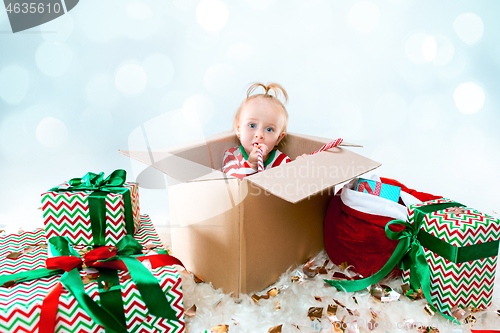 Image of Cute baby girl 1 year old sitting at box over Christmas background. Holiday season.