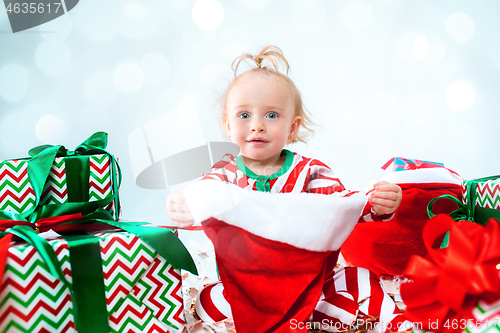 Image of Cute baby girl 1 year old wearing santa hat posing over Christmas background. Sitting on floor with Christmas ball. Holiday season.