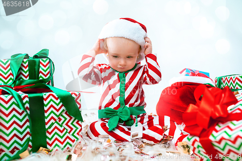 Image of Cute baby girl 1 year old wearing santa hat posing over Christmas background. Sitting on floor with Christmas ball. Holiday season.