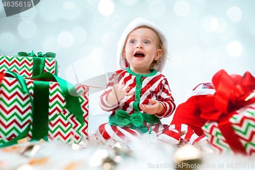 Image of Cute baby girl 1 year old wearing santa hat posing over Christmas background. Sitting on floor with Christmas ball. Holiday season.