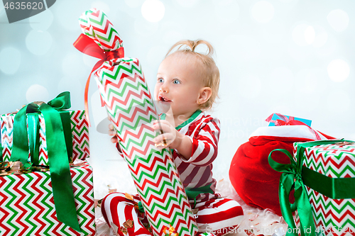 Image of Cute baby girl 1 year old near santa hat posing over Christmas background. Sitting on floor with Christmas ball. Holiday season.