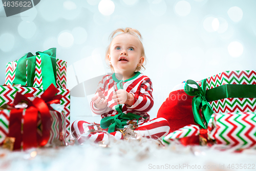 Image of Cute baby girl 1 year old near santa hat posing over Christmas background. Sitting on floor with Christmas ball. Holiday season.