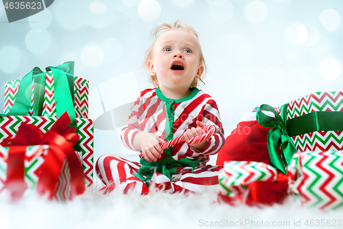 Image of Cute baby girl 1 year old near santa hat posing over Christmas background. Sitting on floor with Christmas ball. Holiday season.