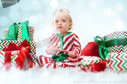 Image of Cute baby girl 1 year old near santa hat posing over Christmas background. Sitting on floor with Christmas ball. Holiday season.