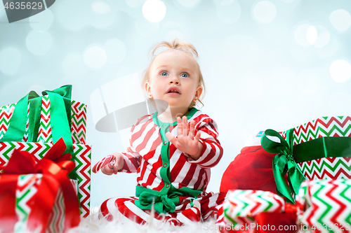 Image of Cute baby girl 1 year old near santa hat posing over Christmas background. Sitting on floor with Christmas ball. Holiday season.