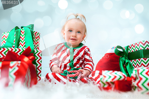 Image of Cute baby girl 1 year old near santa hat posing over Christmas background. Sitting on floor with Christmas ball. Holiday season.