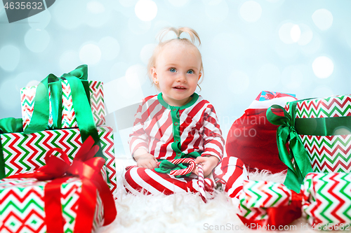 Image of Cute baby girl 1 year old near santa hat posing over Christmas background. Sitting on floor with Christmas ball. Holiday season.