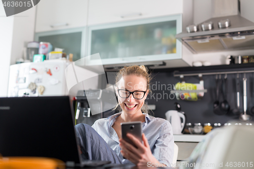 Image of Stay at home and social distancing. Woman in her casual home clothing working remotly from her kitchen dining table in the morning. Video chatting with friend, family or business clients or partners