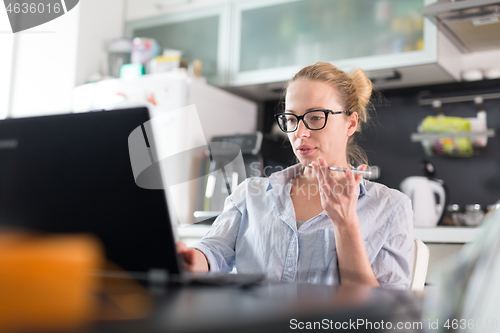 Image of Stay at home and social distancing. Woman in her casual home clothing working remotly from kitchen dining table. Video chatting using social media with friend, family, business clients or partners