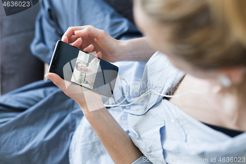 Image of Woman at home relaxing on sofa couch using social media on phone for video chatting with her loved ones during corona virus pandemic. Stay at home, social distancing lifestyle.