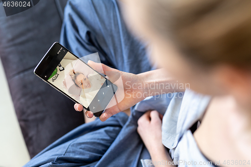 Image of Woman at home relaxing on sofa couch using social media on phone for video chatting with her loved ones during corona virus pandemic. Stay at home, social distancing lifestyle.