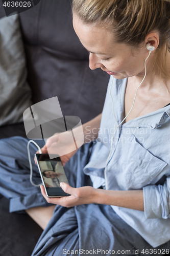 Image of Woman at home relaxing on sofa couch using social media on phone for video chatting with her loved ones during corona virus pandemic. Stay at home, social distancing lifestyle.