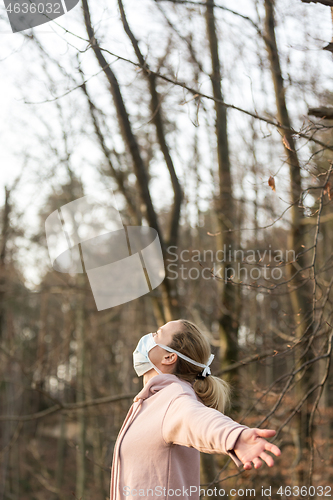 Image of Portrait of caucasian sporty woman wearing medical protection face mask while relaxing by taking a deep breath in forest. Corona virus, or Covid-19, is spreading all over the world