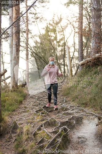 Image of Corona virus, or Covid-19, is spreading all over the world. Portrait of caucasian sporty woman wearing a medical protection face mask while running in nature.