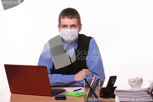 Image of Office specialist in a protective medical mask sits at a desk and looks into the frame