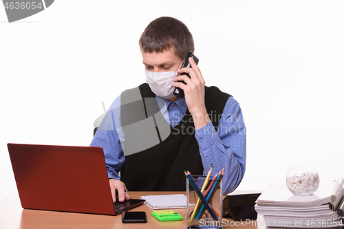 Image of Clerk in a medical mask talking on the phone and working in a computer