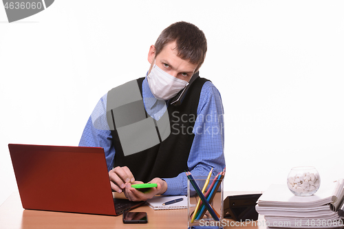 Image of An office worker in a protective medical mask is talking on the phone, counting on a calculator and looking at the frame