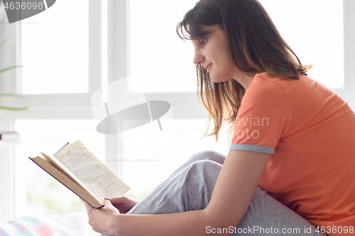Image of Girl at home by the window in the bedroom reads her favorite book