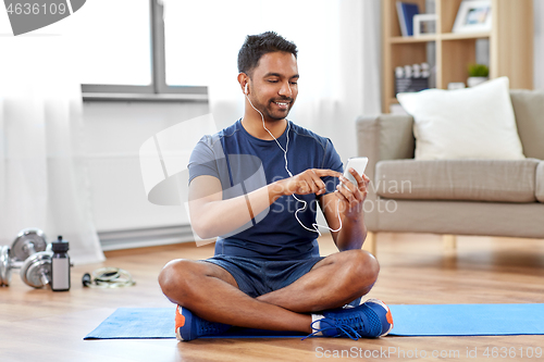 Image of indian man with smartphone on exercise mat at home