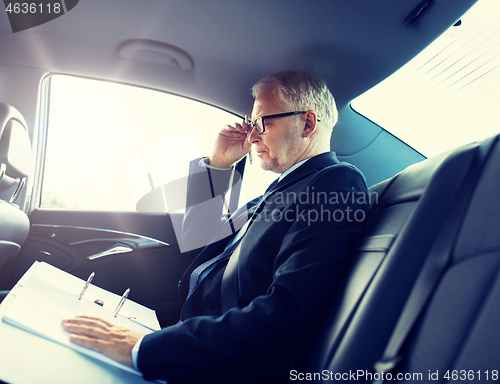 Image of senior businessman with papers driving in car