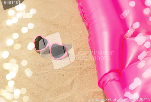 Image of sunglasses and pink swimming mattress on beach