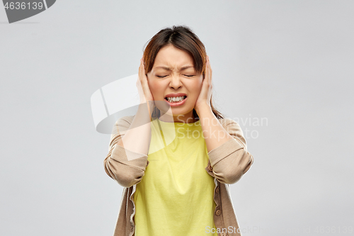 Image of stressed asian woman closing ears by hands