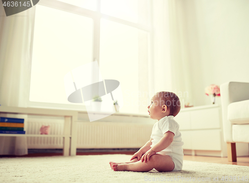 Image of happy baby boy or girl sitting on floor at home