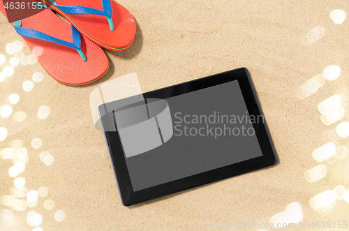 Image of tablet computer and flip flops on beach sand