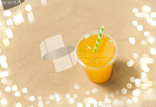 Image of cup of orange juice with straw on beach sand